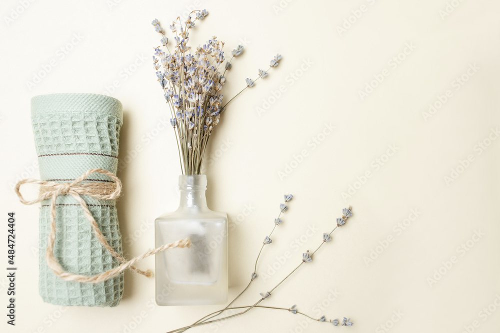The concept of spa salon, bathroom decor, cozy home, feminine. Bouquet of natural dry lavender flowers in a glass bottle, rolled up towel. Top view. Copy space. Beige background.