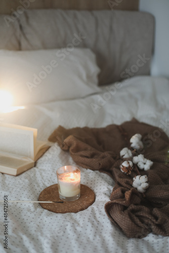 Cozy still life interior details with a book, candle and a cotton twig in warm soft bed. Sweet home