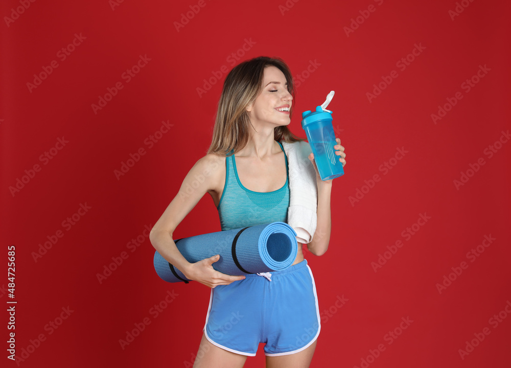 Beautiful woman with yoga mat, towel and shaker on red background Beautiful woman with yoga mat, towel and shaker on red background