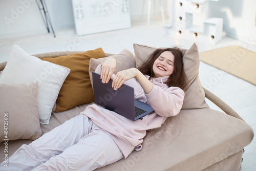 Wide angle of young smiling woman opens the laptop lying on sofa
