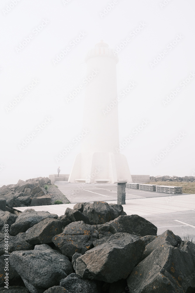 Lighthouse against rough stones and pavement on foggy day