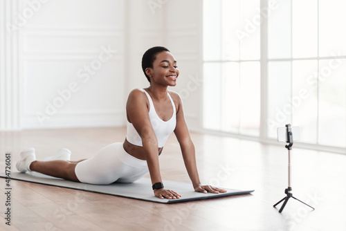 Young african woman stretching back on mat with cellphone