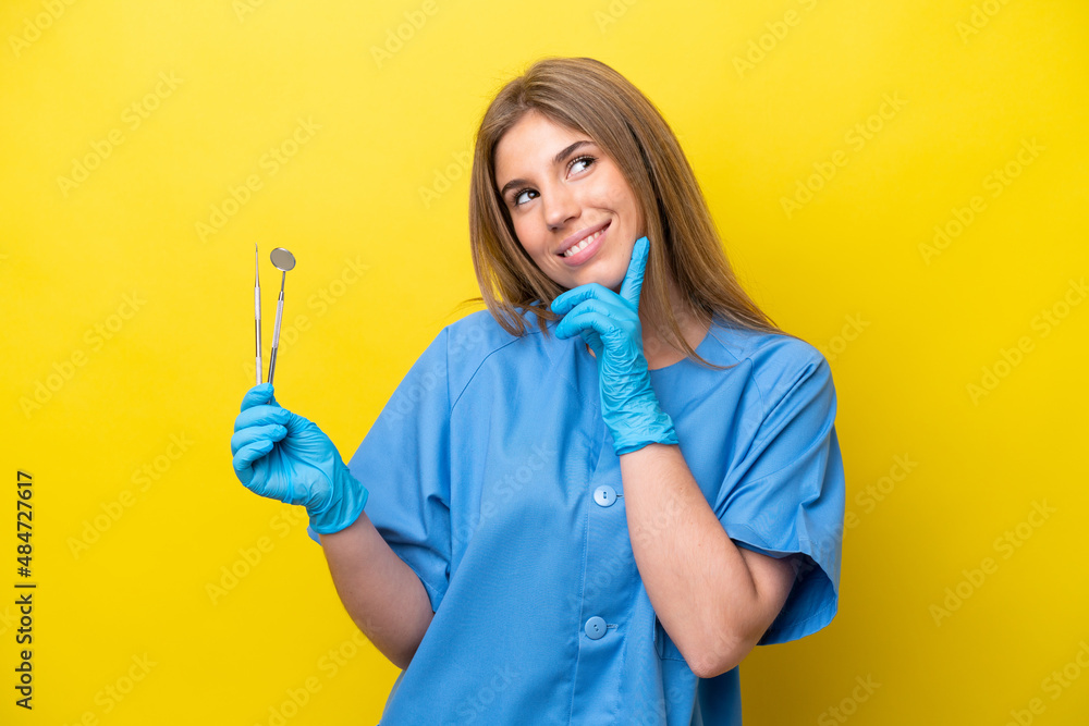 Dentist caucasian woman holding tools isolated on yellow background thinking an idea while looking up Dentist caucasian woman holding tools isolated on yellow background thinking an idea while looking up