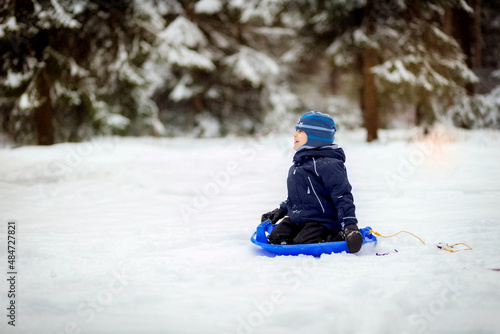 little boy sitting on snow saucer in winter park