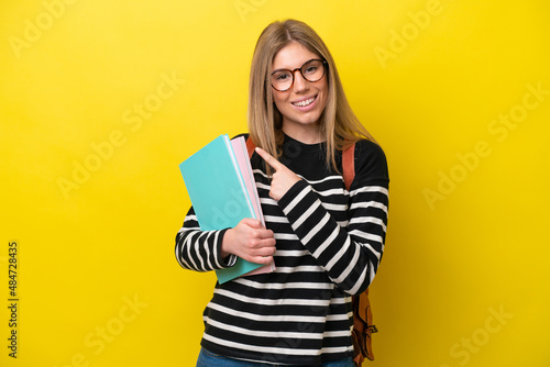 Young student woman isolated on yellow background background pointing to the side to present a product