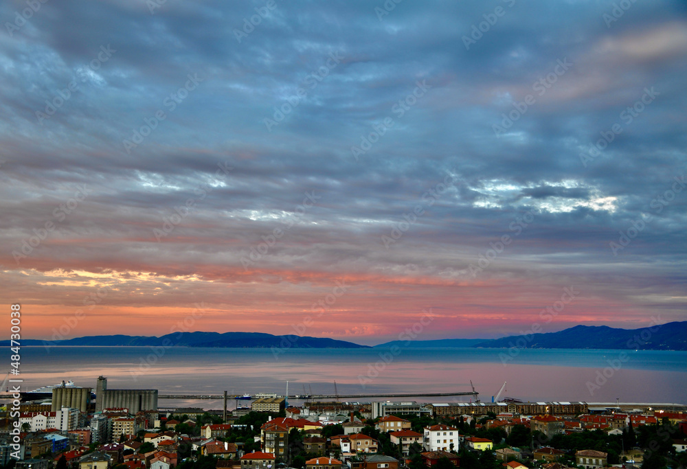 Sky covered with clouds and rijeka gulf in pink summer sunset. Sunset over the city.