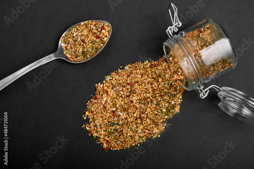 A mixture of various spices in a spoon and poured out of a jar on a black background.