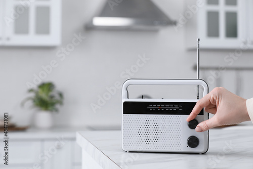 Woman turning volume knob on radio in kitchen, closeup. Space for text photo