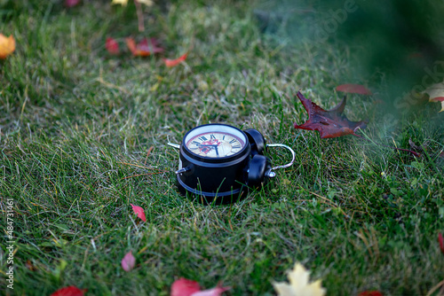 the black alarm clock is lying on the green grass among the autumn leaves