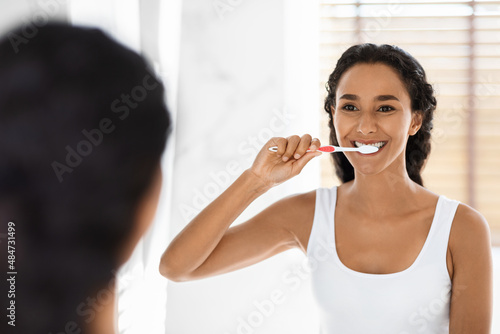 Happy Young Middle Eastern Woman Brushing Her Teeth With Toothbrush In Bathroom