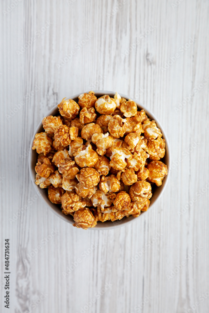 Homemade Caramel Popcorn in a gray Bowl on a white wooden surface, top view. Flat lay, overhead, from above. Space for text. Homemade Caramel Popcorn in a gray Bowl on a white wooden surface, top view. Flat lay, overhead, from above. Space for text.