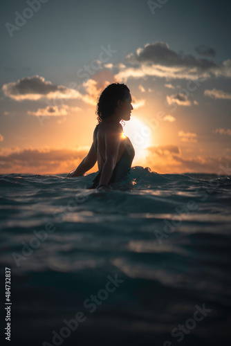 Silueta de mujer joven, latina nadando y disfrutando en el mar al amanecer, a contraluz