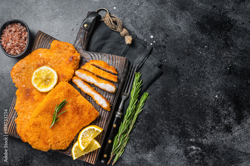 Fried sliced weiner schnitzel on a wooden board with herbs. Black background. Top view. Copy space photo