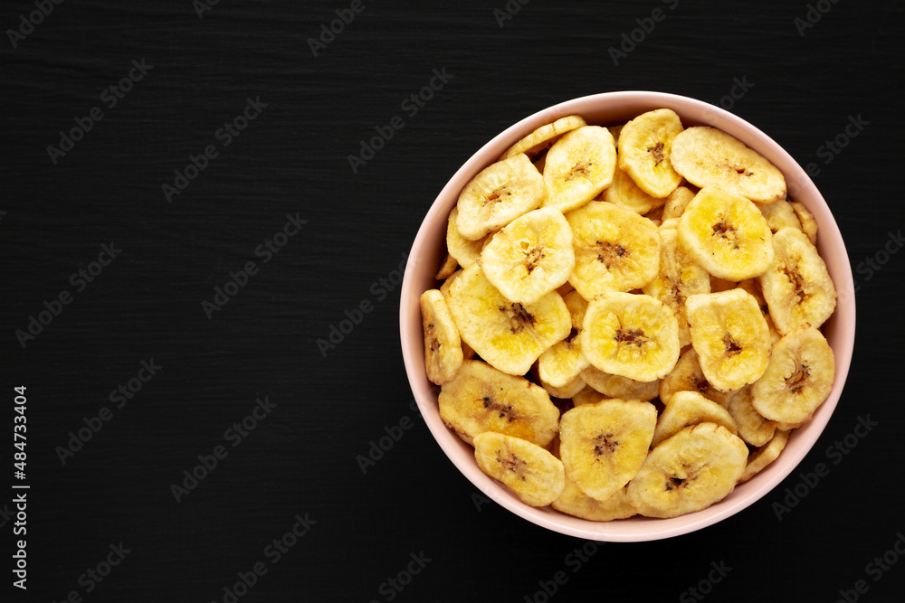 Homemade Banana Chips in a Pink Bowl on a black background, top view. Flat lay, overhead, from above. Space for text.