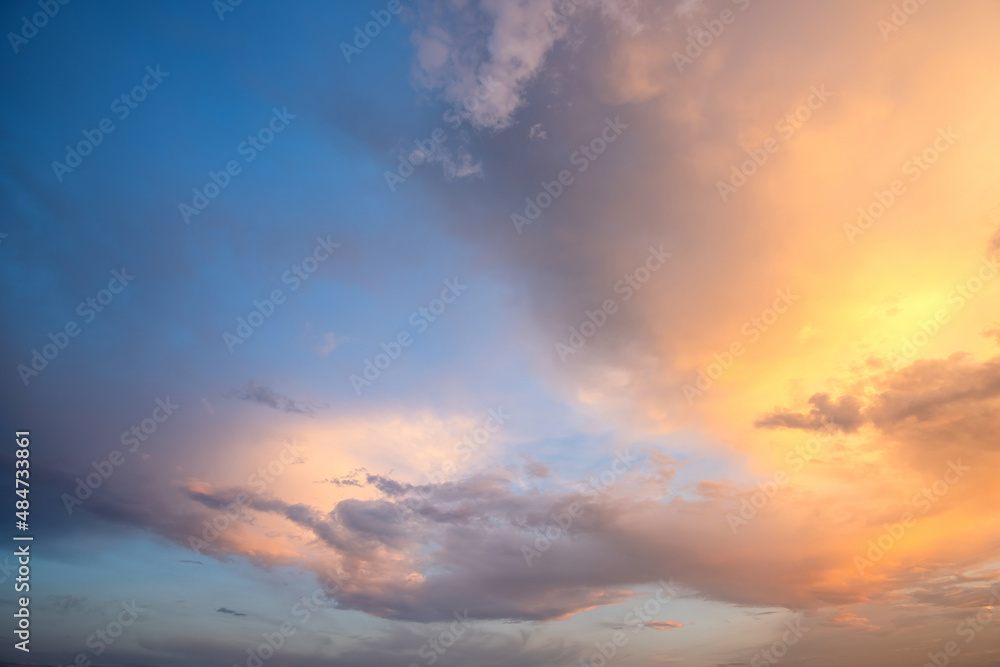 Dramatic sky at sunset with puffy clouds lit by orange setting sun