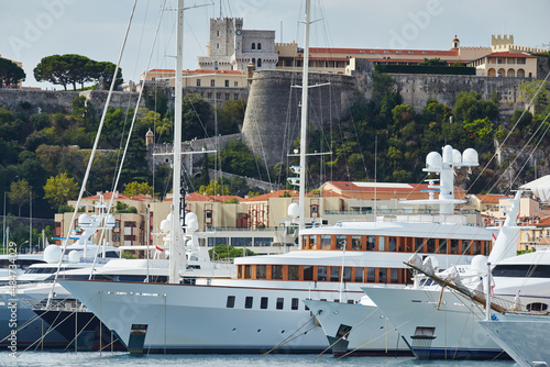 Monaco, Monte-Carlo, a lot of large motor yachts are parked side by side in the port, with huge fenders between them to avoid collision at sunny day, mooring ropes go into the azure water photo