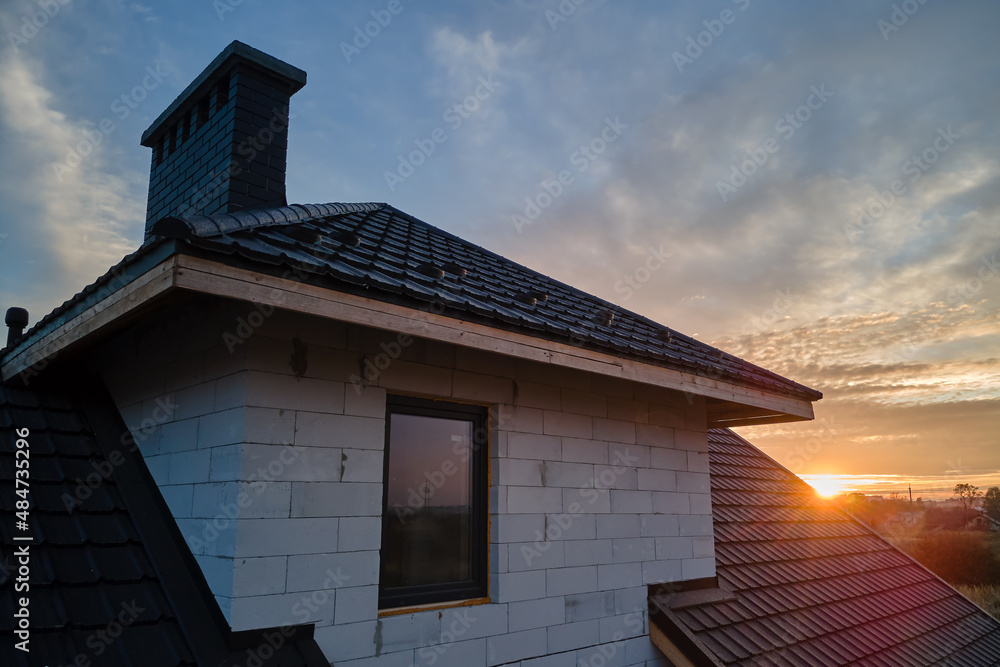 Unfinished house with aerated lightweight concrete walls and wooden roof frame covered with metallic tiles under construction Unfinished house with aerated lightweight concrete walls and wooden roof frame covered with metallic tiles under construction