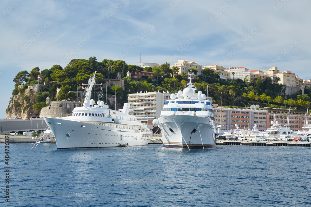 Monaco, Monte-Carlo, two large motor yachts are parked side by side in the port, with huge fenders between them to avoid collision at sunny day, mooring ropes go into the azure water