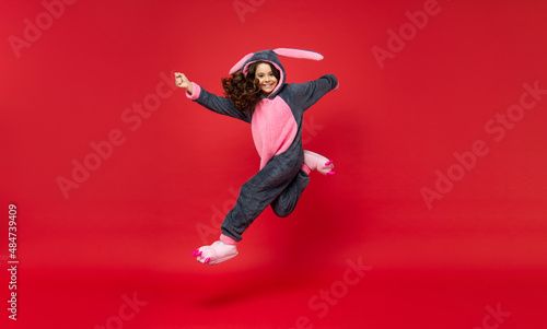 amazed kid in comfortable pajama jumping on red background, full length, comfort