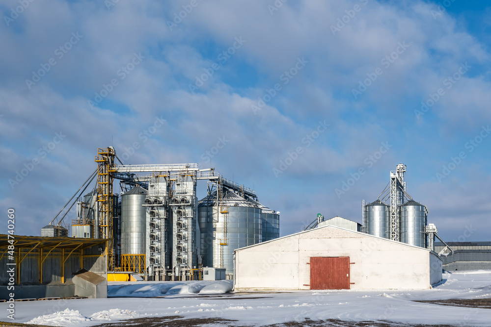 Obraz premium agro silos granary elevator in winter day in snowy field. Silos on agro-processing manufacturing plant for processing drying cleaning and storage of agricultural products, flour, cereals and grain.