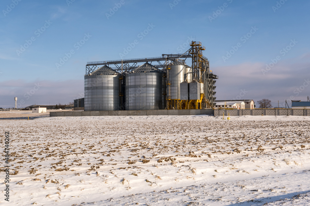 Obraz premium agro silos granary elevator in winter day in snowy field. Silos on agro-processing manufacturing plant for processing drying cleaning and storage of agricultural products, flour, cereals and grain.