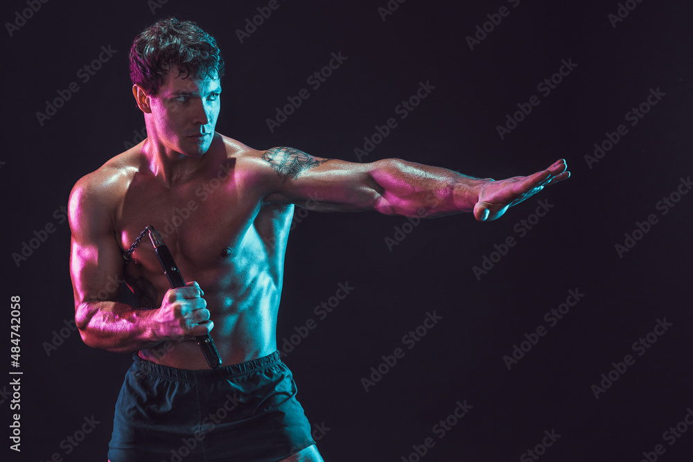Portrait of muscular man who trains with nunchaku while isolated on black background. Sport concept