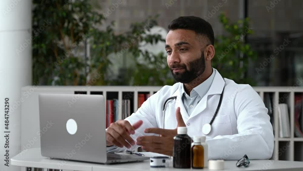 An Indian doctor conducts an online consultation. A general medicine doctor communicates with his patient via a video call using a laptop, prescribes treatment, answers questions,makes recommendations An Indian doctor conducts an online consultation. A general medicine doctor communicates with his patient via a video call using a laptop, prescribes treatment, answers questions,makes recommendations