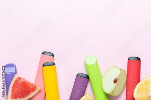 Electronic cigarettes with different fruit flavors with ingredients on colored backgrounds photo