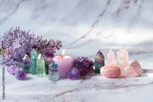 Foto Gemstones minerals, candle, lilac flowers on marble background
