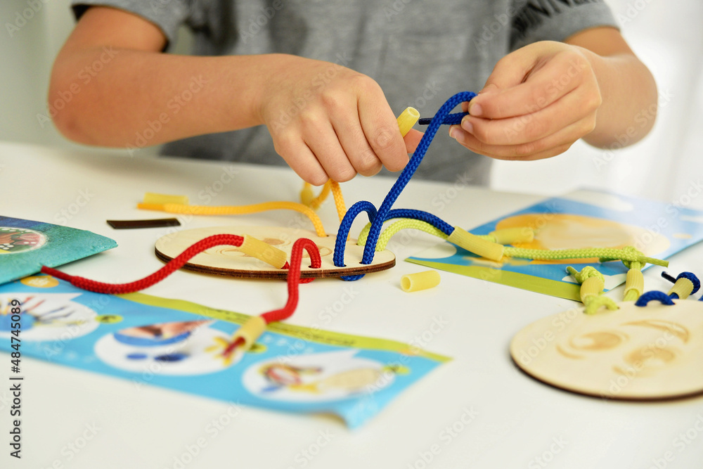 development of fine motor skills. Early education, Montessori Method. Cognitive skills, Children development. Close up of child hands playing with lace or rope and pasta