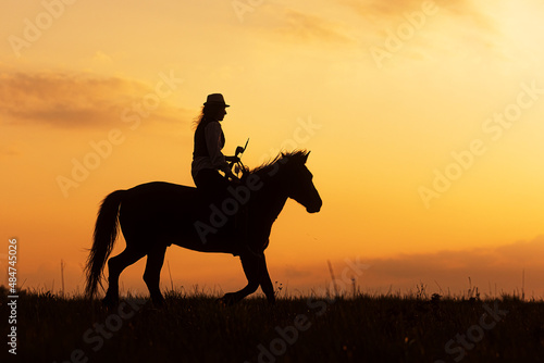 silhouette of a woman riding a horse after sunset © michal