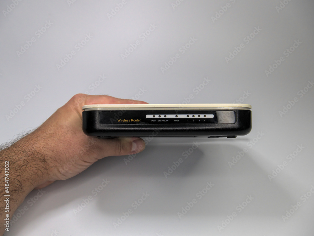 A hand of a person holding wireless internet router against white seamless background, front panel view, copy space A hand of a person holding wireless internet router against white seamless background, front panel view, copy space