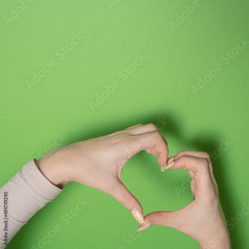 female hand heart shape with shadow against green background. Valentines day. creative adorable decoration idea with copyspace