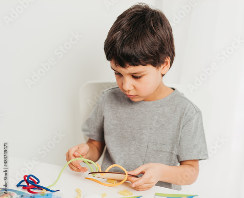 development of fine motor skills. Early education, Montessori Method. Cognitive skills, Children development. Close up of child playing with lace or rope and pasta