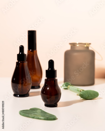 Amber glass spray and dropper bottles with cosmetic on light bathroom table. Natural jade roller for facial massage and Guasha Massage Board. photo