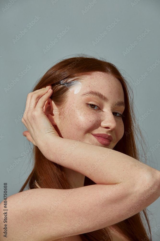 Smiling young beautiful ginger girl use eye lift tapes for fox eyes effect, lifting of eyelids and brows, perfect makeup