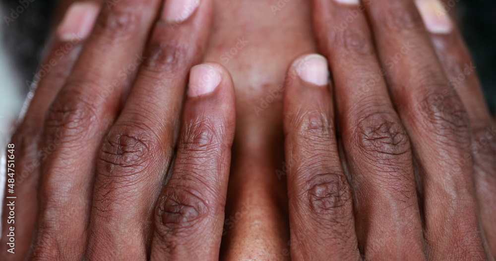 Fototapeta premium Pensive African man covering face with hands, black person revealing eyes portrait thinking