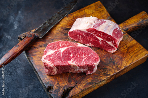 Raw dry aged Angus rib-eye beef steaks offered as close-up on an old rustic wooden board