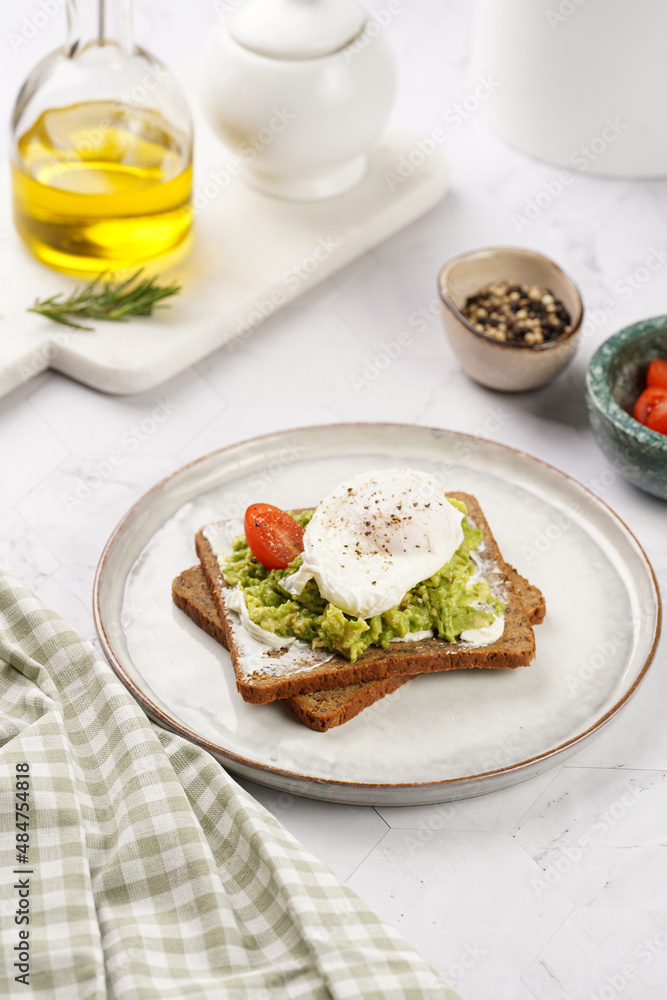 Trendy lifestyle sandwich: protein bread slice with cream cheese, mashed avocado, cherry tomatoes and poached egg on white scandi plate, light setting Trendy lifestyle sandwich: protein bread slice with cream cheese, mashed avocado, cherry tomatoes and poached egg on white scandi plate, light setting