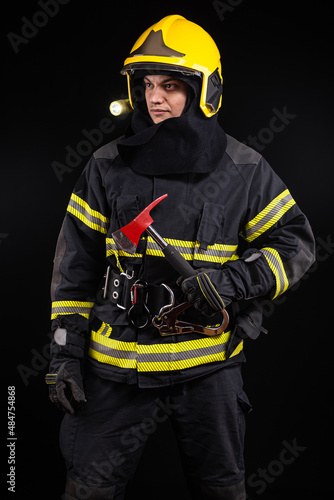 Firefighter fully equipped with helmet and ax in smoke, black background