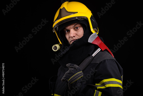 Firefighter fully equipped with helmet and ax in smoke, black background