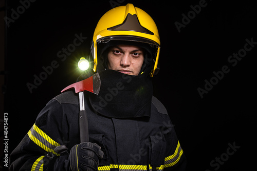 Firefighter fully equipped with helmet and ax in smoke, black background