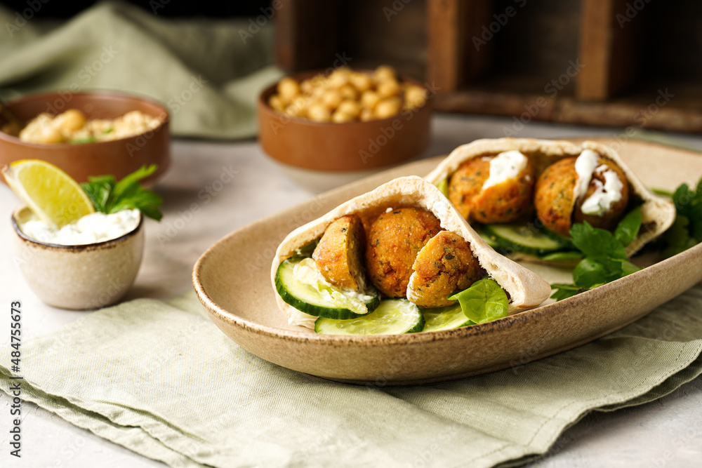 Traditional oriental chickpea deep fried falafel in flatbread pita, tzatziki yoghurt sauce, hummus, fresh lime and green cilantro on light surface Traditional oriental chickpea deep fried falafel in flatbread pita, tzatziki yoghurt sauce, hummus, fresh lime and green cilantro on light surface