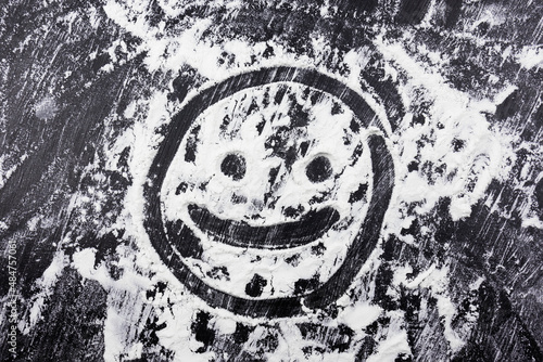 Smiling face drawn with finger on flour scattered on black table