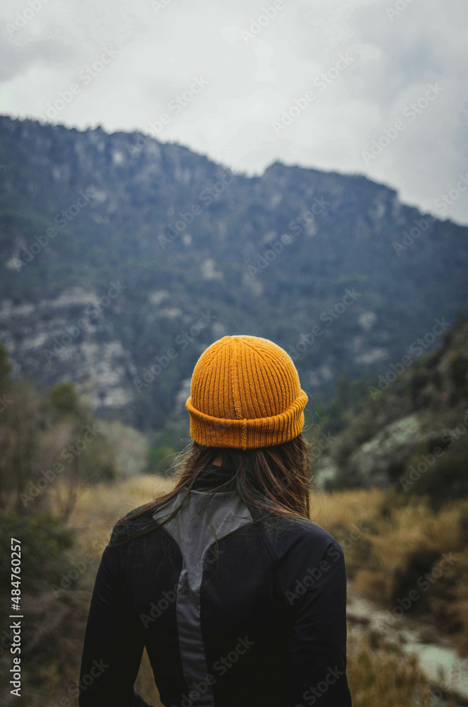 Inspiring Vertical Picture of Blonde Woman with Yellow Hat Standing Looking at Nature Background From Behind