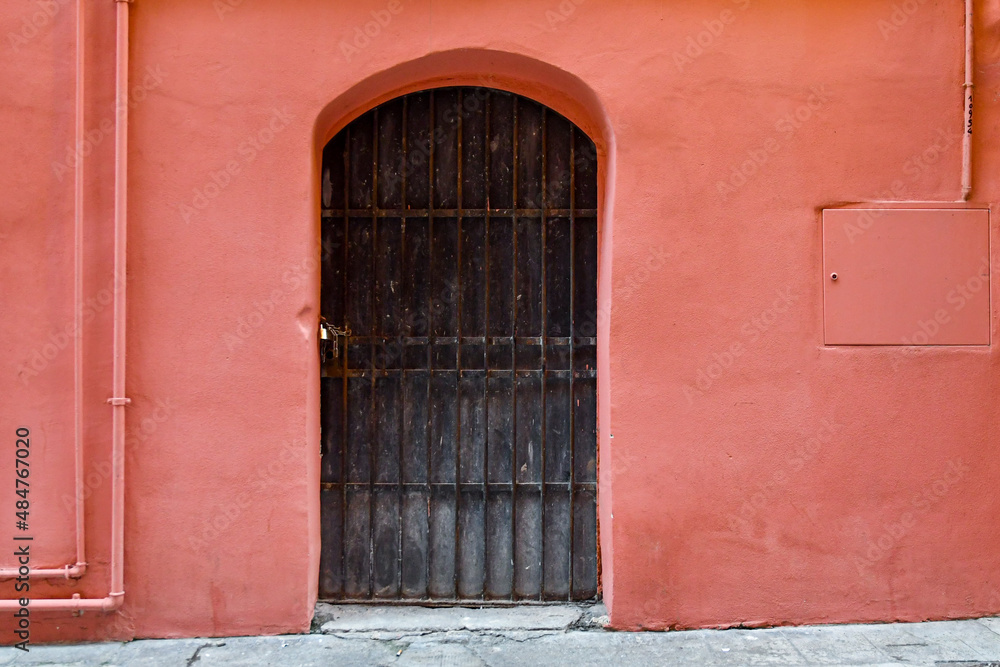 Black metal arch door closed with chain and padlock on the bright pink wall of an old house in the old town of Sanremo, Imperia, Liguria, Italy

