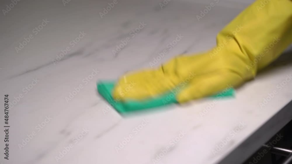 A housewife in yellow rubber gloves washes and wipes a marble kitchen countertop A housewife in yellow rubber gloves washes and wipes a marble kitchen countertop