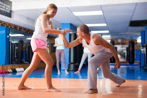 Concentrated young female practicing effective self defence techniques with coach in training room