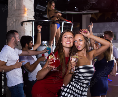 Cheerful females friends with drinks dancing in the club on party