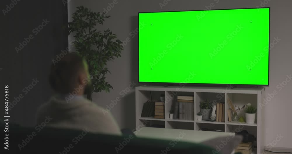 Back view of man in casual wear sitting on couch at living room and watching TV with chroma key screen. Relaxation at home with new movie. Back view of man in casual wear sitting on couch at living room and watching TV with chroma key screen. Relaxation at home with new movie.